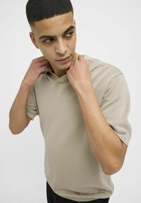 Beige polo-shirt met korte mouwen en v-hals ontwerp, met een relaxte pasvorm en een soepele textuur, gedragen door iemand die de kraag aanpast.