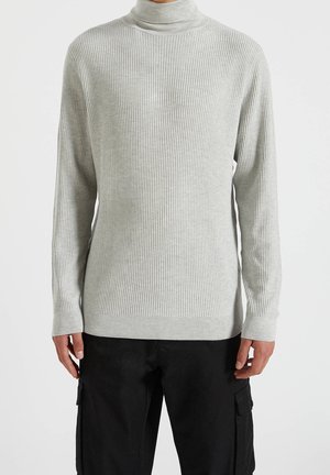 Suéter de cuello alto de canalé en gris claro con mangas largas y puños ajustados. Textura suave y silueta esbelta. Combinado con pantalones cargo negros.