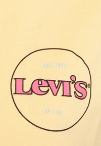 Gul tyg med en rund grafisk logotyp som har "Levi's" i rosa, "EST. 1873" och "SF / CA" i blått, omgiven av svart.