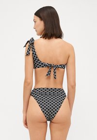Fekete-fehér mintás bikini, egy vállpántos toppal, masnis záródással és magas derekú alsó résszel. Simaságot és minimalista dizájnt kínáló anyag.