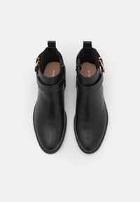 Bottines en cuir noir avec une texture lisse, bout rond et accent de boucle sur le côté. L'intérieur est doté d'une semelle intérieure beige avec un logo.