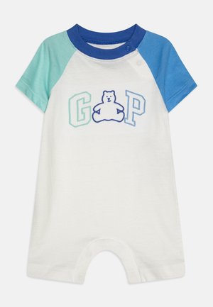 Biały kombinezon niemowlęcy z niebieskimi i turkusowymi rękawami typu raglan, niebieskim kołnierzykiem oraz haftowanym misiem między literami "G" i "P" na piersi.