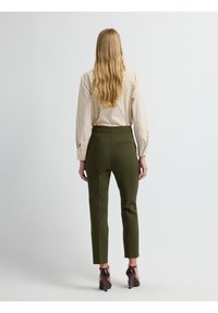 Chique, lichtbeige blouse met lange mouwen en knoopdetails, gecombineerd met olijfgroene slim-fit broek, enkellang, met een achterzak.