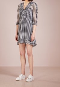 Vestido de cuadros en blanco y negro con escote en V, con volantes, mangas tres cuartos y un dobladillo acampanado. Combinado con zapatillas blancas.