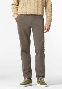 Pantalons en coton marron à coupe slim avec poches latérales, associés à des baskets en suède vert olive et un pull en maille beige.