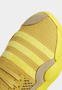 Baskets tricotées jaunes avec trois bandes jaunes plus claires, empiècements en daim beige et semelle en caoutchouc jaune vif.