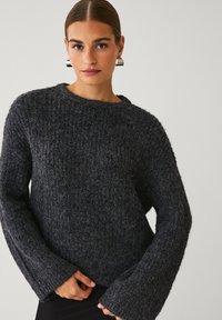 Chunky mørkegrå sweater med et tekstureret strik, brede klokkeærmer og en rund halsudskæring, der har en løs pasform og blødt stof.