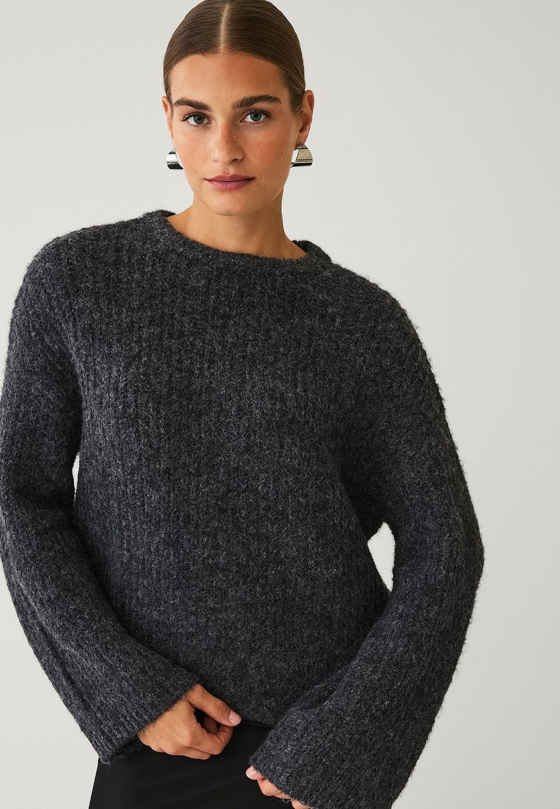Chunky mørkegrå sweater med et tekstureret strik, brede klokkeærmer og en rund halsudskæring, der har en løs pasform og blødt stof.