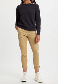 Sweatshirt gris foncé avec un col rond, associé à un chino beige clair et des baskets montantes blanches, présentant une coupe décontractée et un ourlet retroussé.