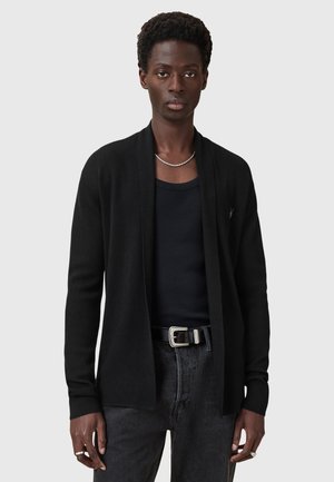 Cardigan noir ouvert à l'avant avec des manches longues, texture côtelée et coupe décontractée, porté sur un débardeur noir et un jean foncé.