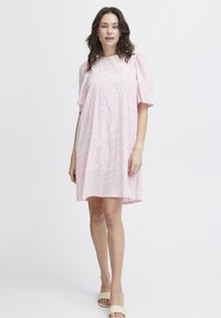 Vaaleanpunainen mekko, jossa on hienovarainen kuvio, lyhyet puff-hihat ja rento istuvuus, jossa on pyöreä pääntie ja polven ylle ulottuva pituus. Sujuva kangas.