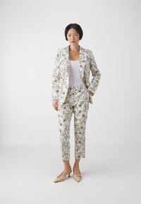 Blomstermønstret dress laget av lett stoff, med en tettsittende blazer og cropped bukser i nyanser av hvitt, grønt og svart.
