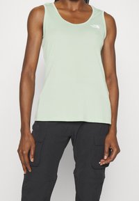 Ljusgrön ärmlös tanktopp i mjukt tyg med rundad halsringning och logodetalj på bröstet. Enkel, figurnära design.