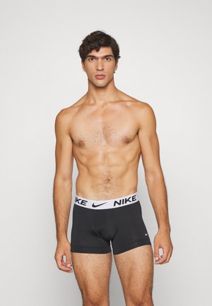 Schwarze Boxer-Briefs mit einem weißen Nike-Logo am Bund; glattes Material, figurbetontes Design, Länge bis zur Mitte des Oberschenkels. Keine zusätzlichen Details oder Muster.