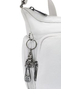 Borsa sintetica bianca con una grande tasca con zipper, portachiavi metallico con un ciondolo a forma di robot e una superficie strutturata.