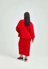 Rotes Sweatshirt- und Rock-Set, mit langen Ärmeln, lockerer Passform und einem Seitenschlitz am Rock. Getragen mit roten und beigen Sneakers.