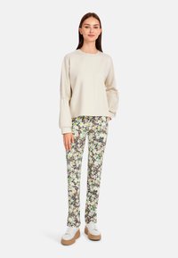 Hellbeige Pullover mit überschnittenen Schultern, kombiniert mit eng anliegenden Hosen mit einem Blumen- und Tierdruck. Weiße Sneaker mit einer sandfarbenen Sohle.