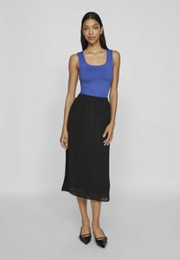 Niebieski top bez rękawów, czarna plisowana spódnica midi i czarne płaskie buty z czubkiem. Gładki materiał topu, fakturowane plisowania na spódnicy, dopasowany pas.