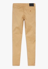 Beige farkkukankaiset housut, joissa on kapea malli. Vyötäröllä on musta nahkapläntä ja takataskussa napillinen suljenta.