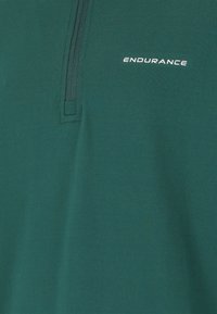 Grön zip-up tröja i mjukt tyg, med en halv dragkedja och ordet "ENDURANCE" i vit tryck på vänster sida.