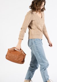 Beige Strickpullover, hellblaue hochgeschnittene Jeans und eine braune Ledertasche mit strukturierter Oberfläche und kurzen Griffen.