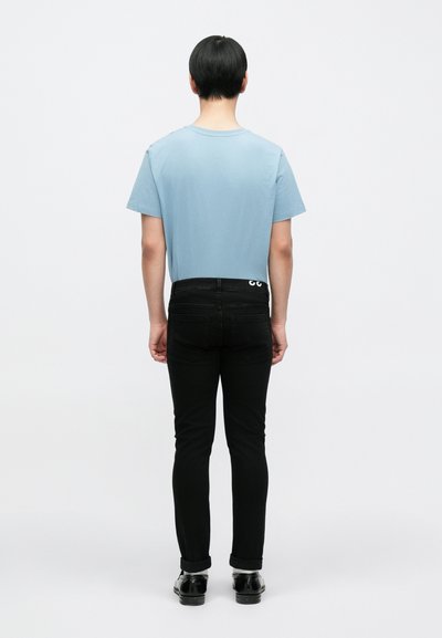 Ανοιχτό μπλε βαμβακερό μπλουζάκι με κοντά μανίκια, συνδυασμένο με μαύρο τζιν παντελόνι. Το τζιν διαθέτει κεντημένη ετικέτα λογότυπου στην πίσω τσέπη.