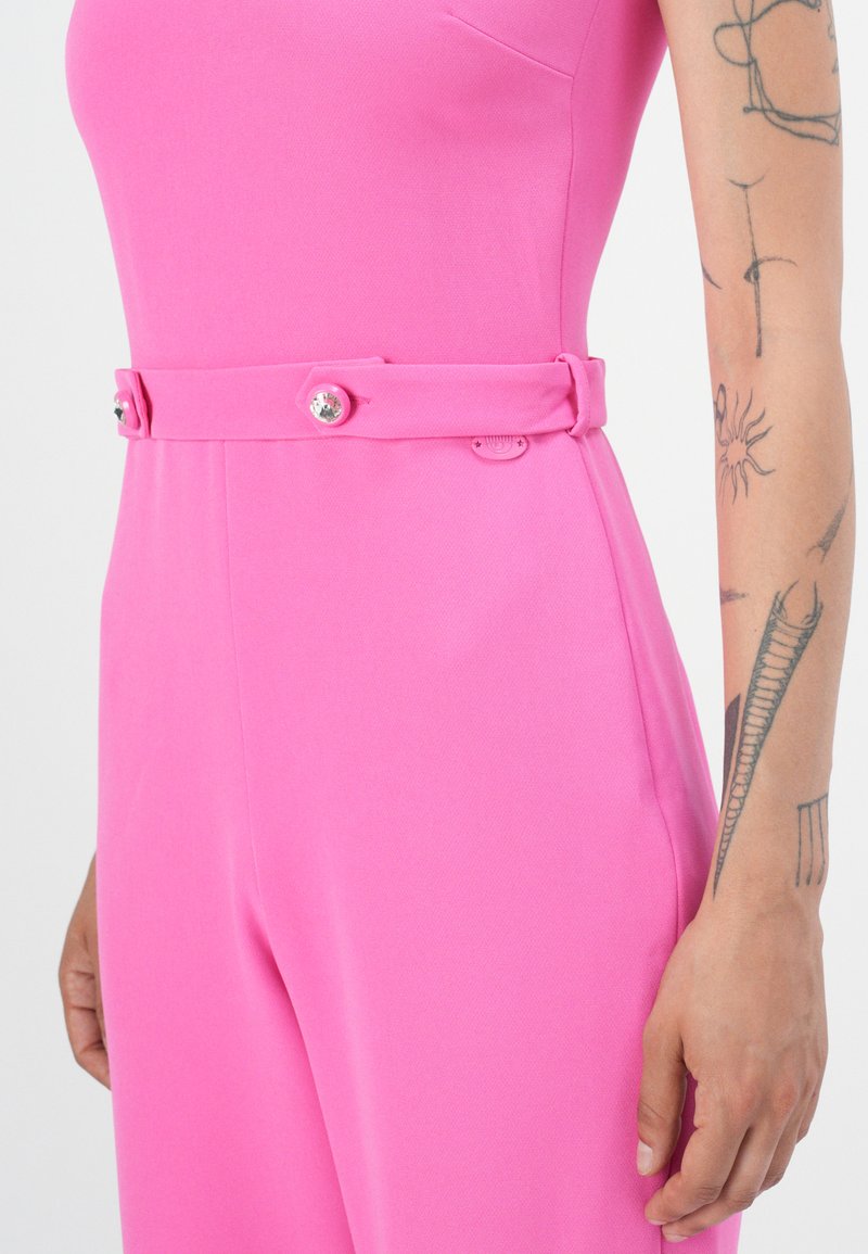 Getailleerde roze jumpsuit met een brede riem, voorzien van twee knopen en een gestructureerde textuur. Opvallende stikseldetails langs de naden.