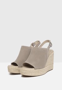 Beige wedge sandals with a textured upper, open-toe design, and an adjustable ankle strap. Espadrille-style jute-wrapped sole.