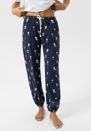 Person wearing navy blue pajama pants with elastic ankles and white drawstring, decorated with small Snoopy and Peanuts character prints.
