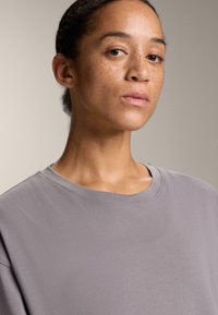 Sivé tričko s krátkym rukávom z jemnej látky, s okrúhlym výstrihom a voľným strihom. Hladká textúra s minimálnymi švami.