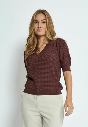Bordeauxfarbener Strickpullover mit V-Ausschnitt, der ein strukturiertes Wellenmuster und kurze Ärmel aufweist. Kombiniert mit hellen Hosen.