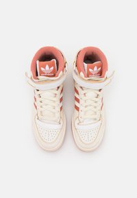 High-top Adidas sneakers featuring white leather, coral accents, perforated toe, and padded collar with logo on tongue and strap.