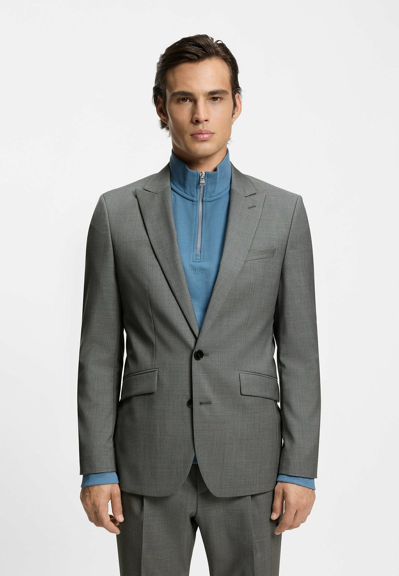 Gråt skræddersyet jakkesæt med hakket revers og en blåt lag med lynlås indeni. Jakkesættet har et tekstureret stof og er kombineret med en blå top under.