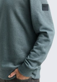 Lichtgroene sweatshirt met een zachte textuur, ribgebreide manchetten en onderrand, met een klein zwart label op de linkerschouder.