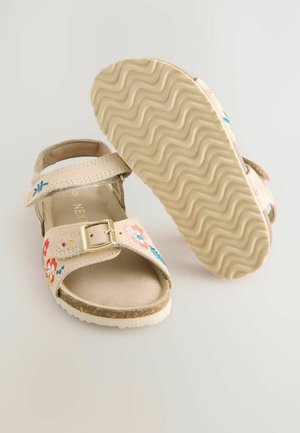Sandales beiges avec broderie florale en rose et bleu, sangles ajustables, détail de boucle et semelle en caoutchouc texturée et ondulée.