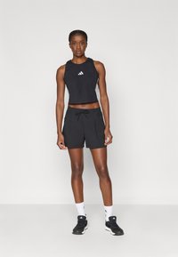 Svart cropped treningsgenser med hvit logo og sidestriper, kombinert med svarte shorts med snøring og sidelommer. Inkludert sorte joggesko.