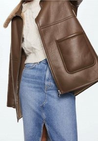 Giacca di pelle marrone con colletto in pelliccia, caratterizzata da due grandi tasche frontali, abbinata a una gonna in denim azzurro chiaro con uno spacco frontale.