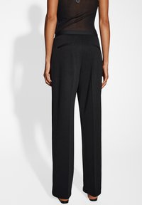 Pantalons plissés noirs avec une coupe ajustée. Comprend des poches arrière et une texture de tissu lisse, présentant un design minimaliste.