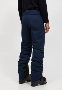 Marineblauwe waterdichte skibroek met een slim fit, voorzien van een verstelbare tailleband, versterkte manchetten en zwarte accenten bij de enkels.