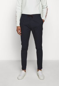 Navy jogger pants with drawstring waist, tapered leg, and side pockets, paired with a white sweatshirt and white sneakers.