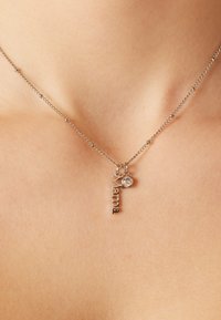 Zilveren ketting met een hangende hanger met het woord "Mama" en een kleine kristalaccent, weergegeven tegen een huidtint achtergrond.