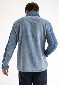 Sudadera de forro polar azul con un cuerpo texturizado y mangas suaves. Presenta un alto cuello y un ajuste relajado. Diseño clásico adecuado para superponer.