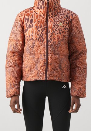 Doudoune orange et marron à imprimé léopard avec col haut portée sur un legging noir Adidas avec logo sur la cuisse gauche.