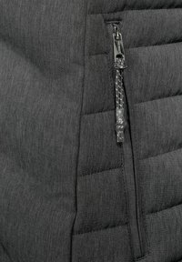 Grå pufferjacka i tyg med kviltad textur. Har en dragkedjeficka med en genomskinlig plastdragrem och en svart dragkedja.