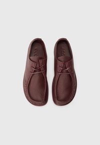 Mørk burgunder lær slip-on-sko med teksturerte overflater, dobbel søm og rund tådesign. Merkevarelogoen er preget på sålen.