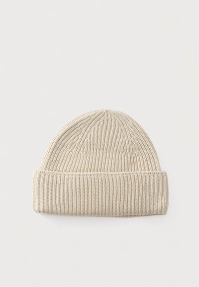 Gorro beige tejido con patrón acanalado y puño doblado sobre un fondo liso y claro.