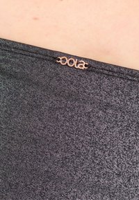 Svart, strukturerad tyg med metallisk glans som har en liten kopparfärgad logotagg. Designen har en slät, åtsittande silhuett.