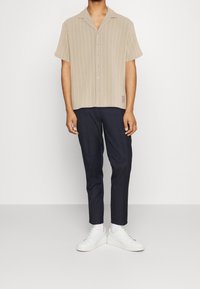 Maglietta a maniche corte corta con righe bianche verticali, abbottonata, abbinata a pantaloni scuri e sneakers bianche. Tessuto con una sottile trama.