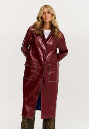 Bordowy winylowy długi płaszcz z kołnierzem, z przodu na guziki, dwoma kieszeniami naszytymi, kontrastowym białym ściegiem i rozcięciem u dołu.