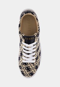 Beżowo-czarne sportowe buty w wzory z białymi sznurowadłami, złotymi oczkami i czarnym językiem oznaczonym napisem "GUESS" w złotej czcionce.